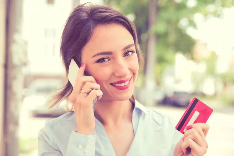 Mujer llamando por teléfono con una tarjeta bancaria en la mano